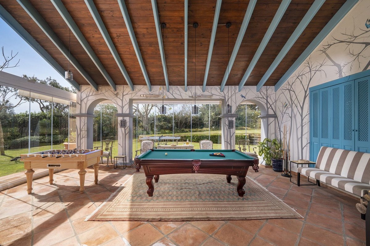 Spacious sunroom with pool table and foosball table, featuring large windows overlooking a garden.