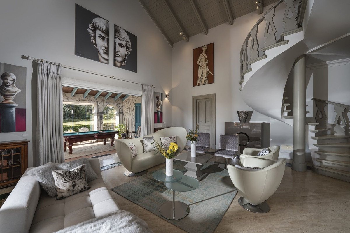 Spacious living room with modern sofas, a spiral staircase, art, and a view to a pool table and garden.