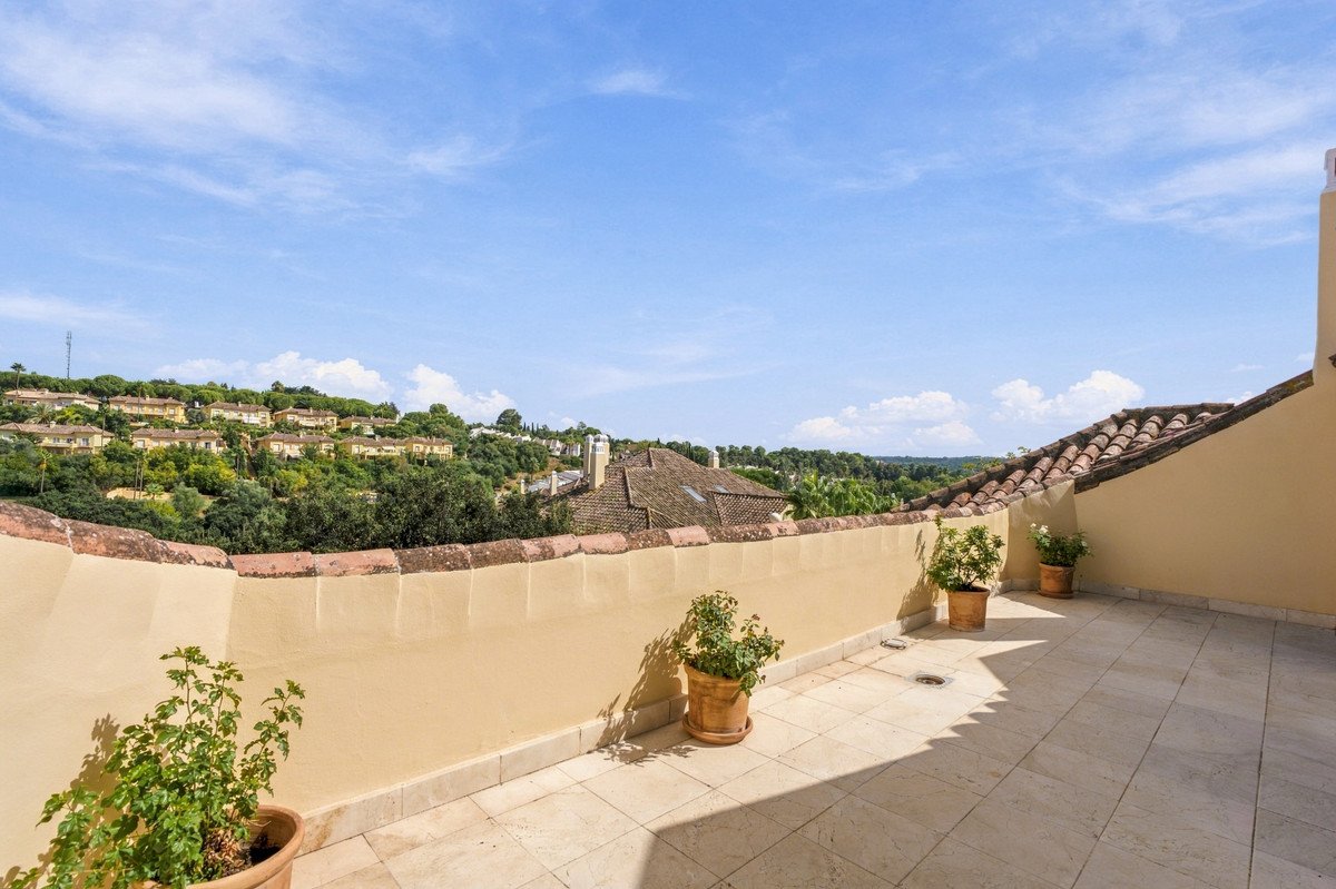 Spacious terrace with potted plants offering a view of hillside villas under a clear blue sky.