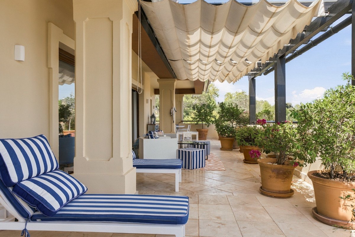 Terrace with blue and white striped lounge chairs, potted plants, and a retractable awning providing shade.