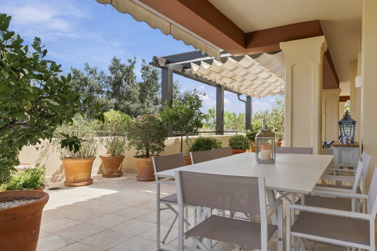 Spacious terrace with a dining table, chairs, and potted plants overlooking a lush garden under a retractable awning.