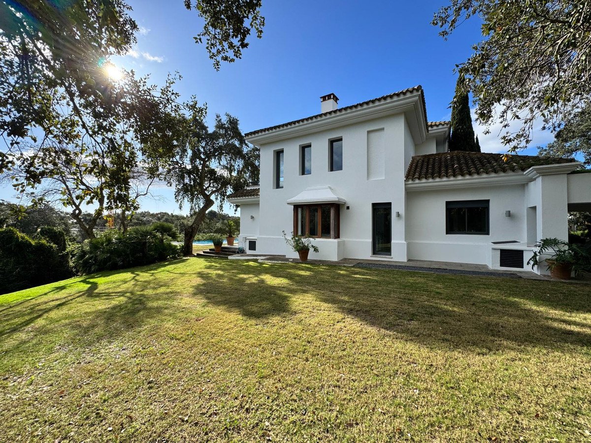 Exterior of a white house with a large green lawn, trees, and a glimpse of a swimming pool in the background.