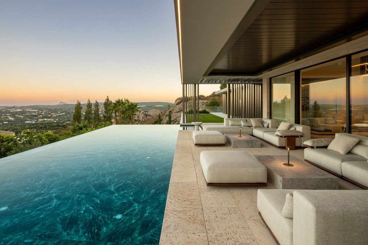 Modern infinity pool and spacious outdoor lounge area with large sectional sofas overlooking a scenic valley at sunset.