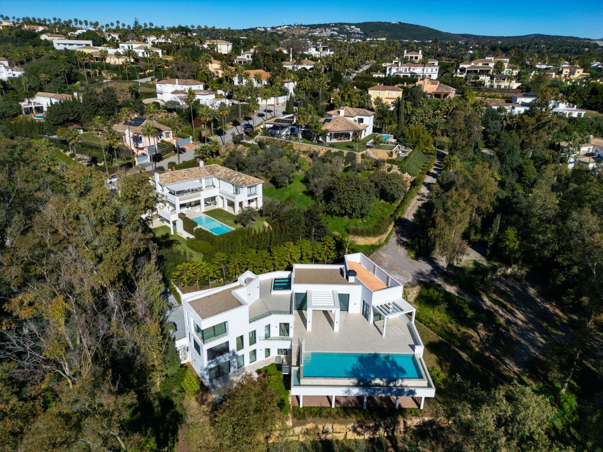 Aerial view of a modern white villa with a swimming pool and surrounding greenery in a residential estate.
