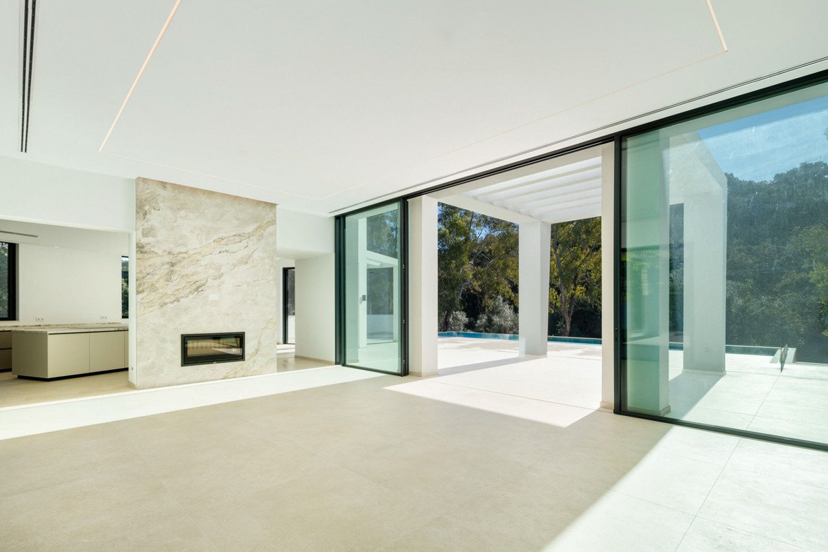 Spacious modern living room with marble fireplace, large sliding glass doors opening to a covered patio and pool area, overlooking trees.