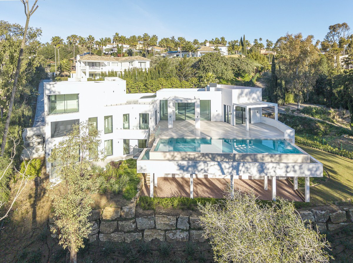 Modern white villa with infinity pool and spacious terrace overlooking lush green hills.
