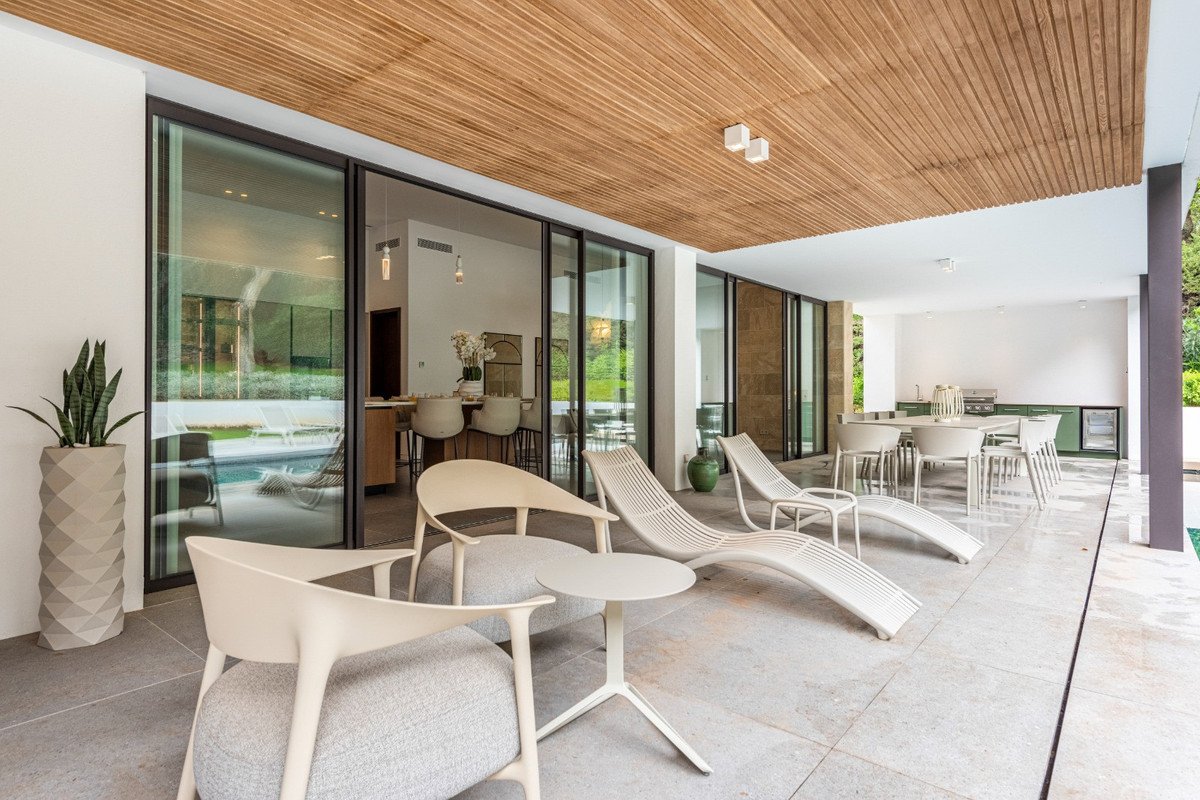 Modern covered patio with lounge chairs, dining table, and outdoor kitchen, overlooking a swimming pool.
