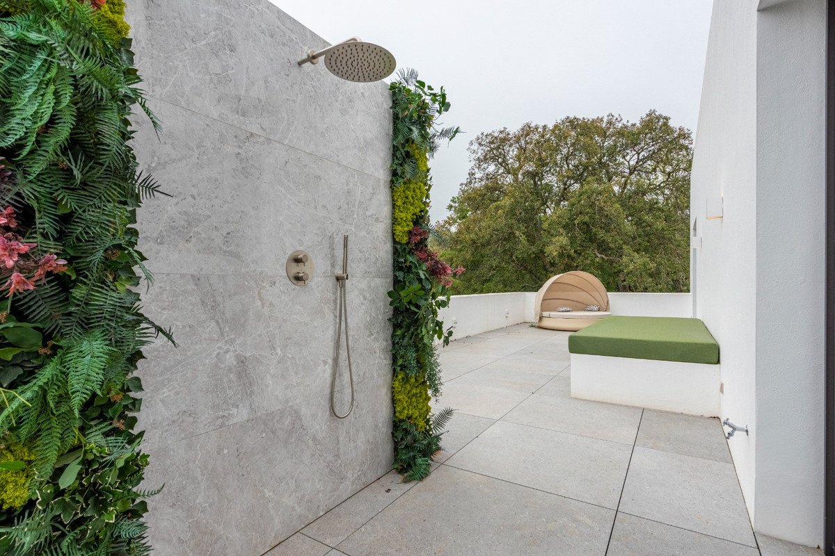 An outdoor shower with a vertical garden feature on a stone wall, overlooking a terrace with seating and greenery.