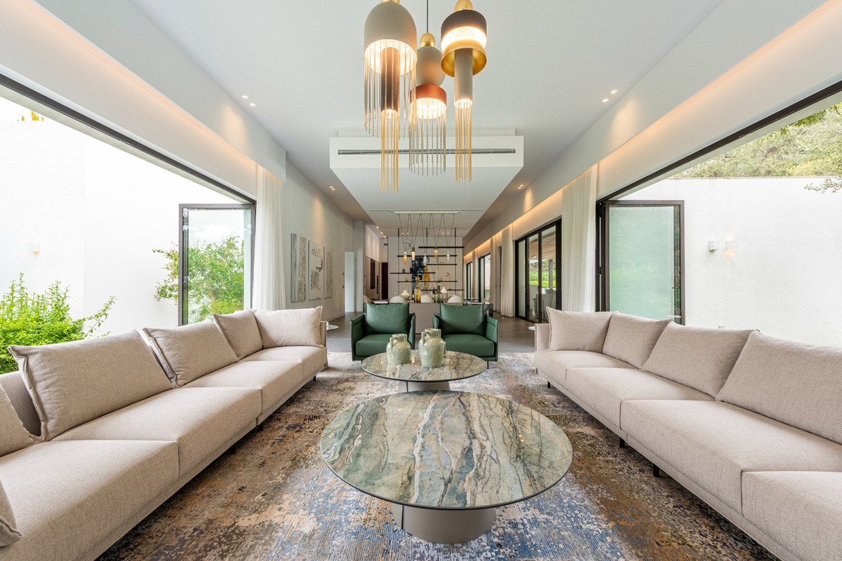 Spacious modern living room with large sofas, two coffee tables, green armchairs, and open glass doors leading to an outdoor view.