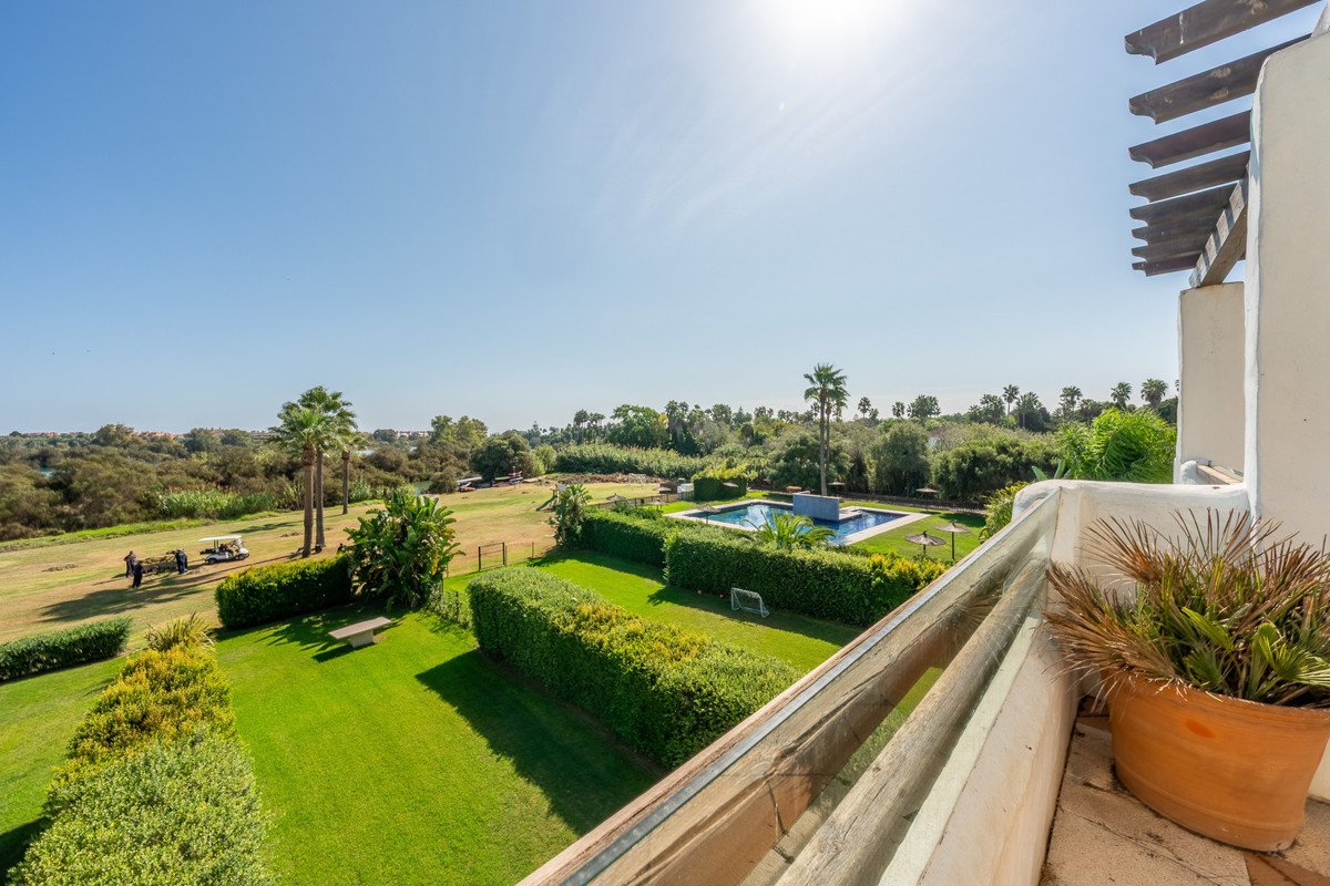 A sunny view from a balcony overlooking a lush golf course with a swimming pool and palm trees.
