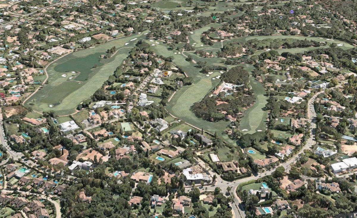 Aerial view of a luxury residential area with golf courses and private villas, featuring lush greenery and swimming pools.