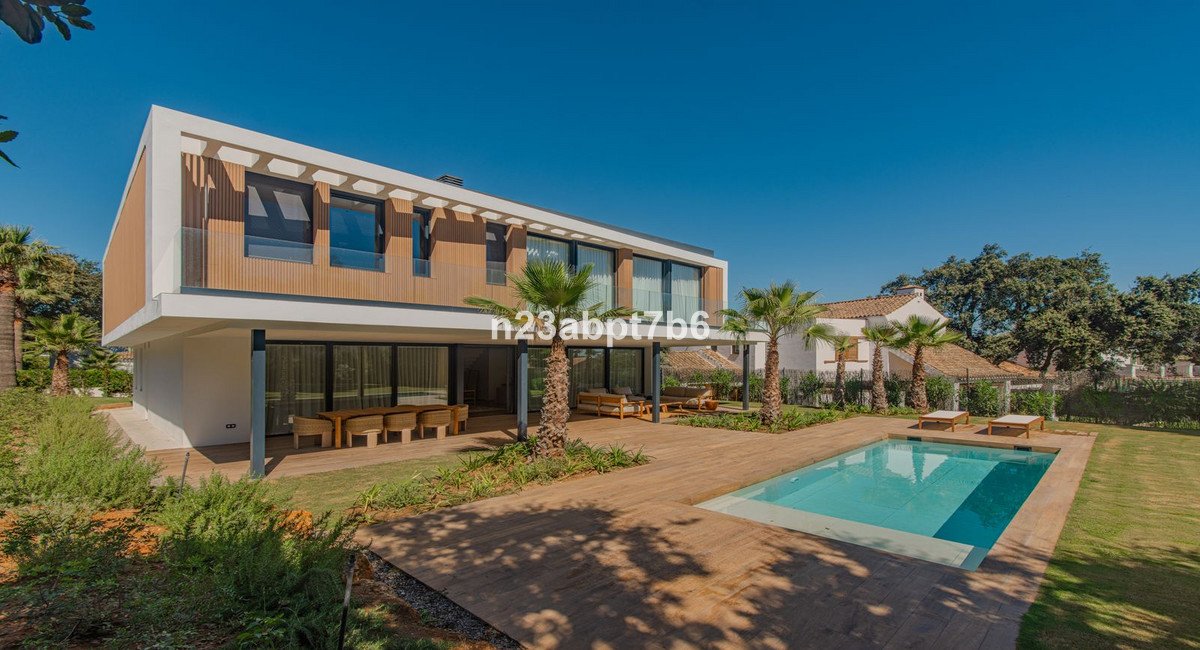 Modern villa with pool, outdoor dining area, and lush green lawn on a sunny day.