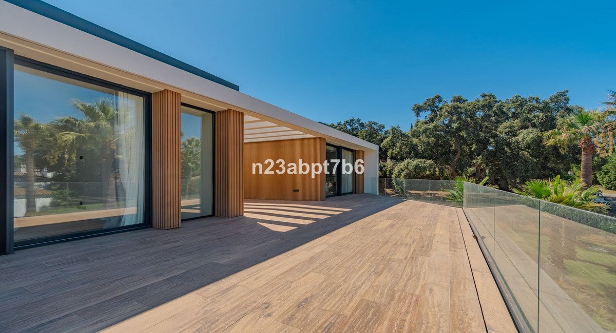 Modern terrace with wooden floor and glass railing, overlooking lush trees and palm trees under a clear blue sky.