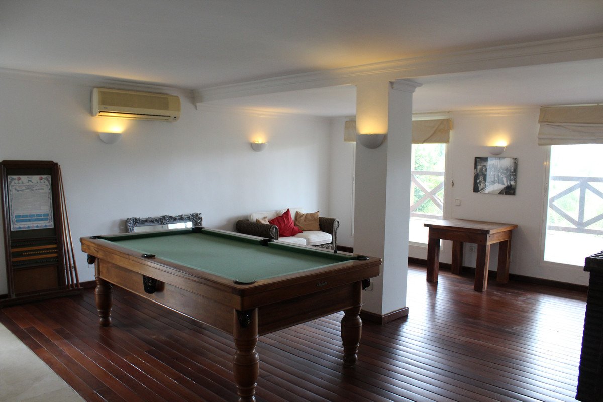 A recreation room featuring a pool table, a sofa with cushions, and natural light from windows with white decorative lattices.