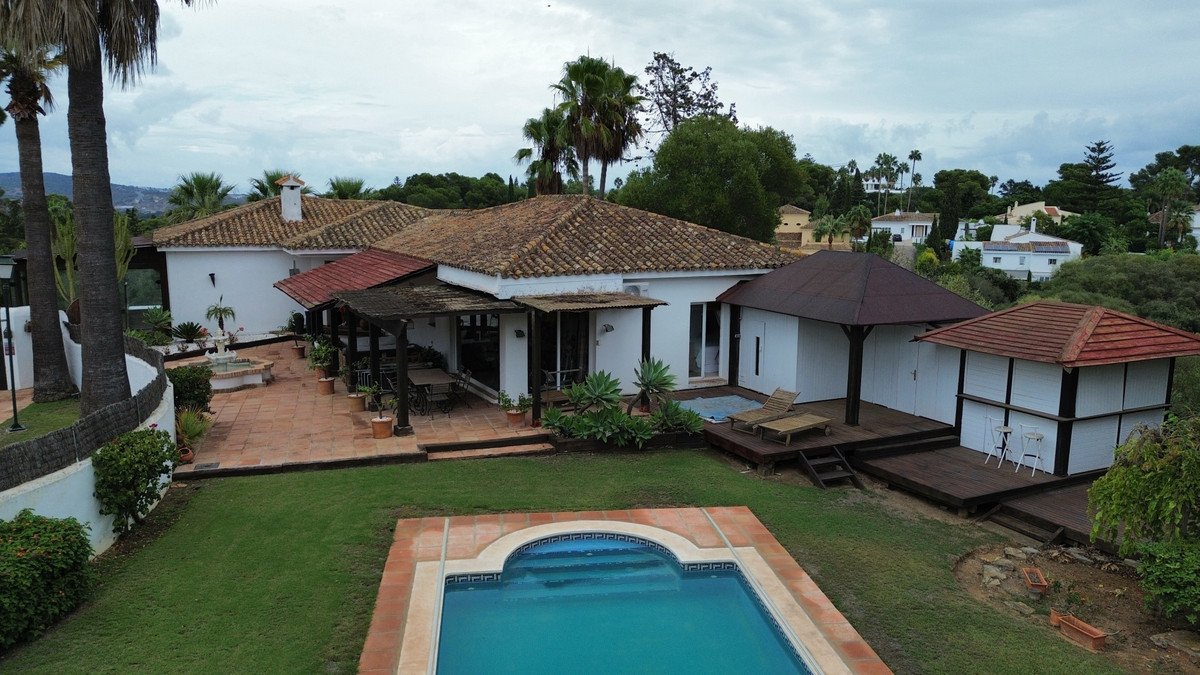 A white villa with a tiled roof, featuring a swimming pool, garden, outdoor dining area, and a separate modern structure.