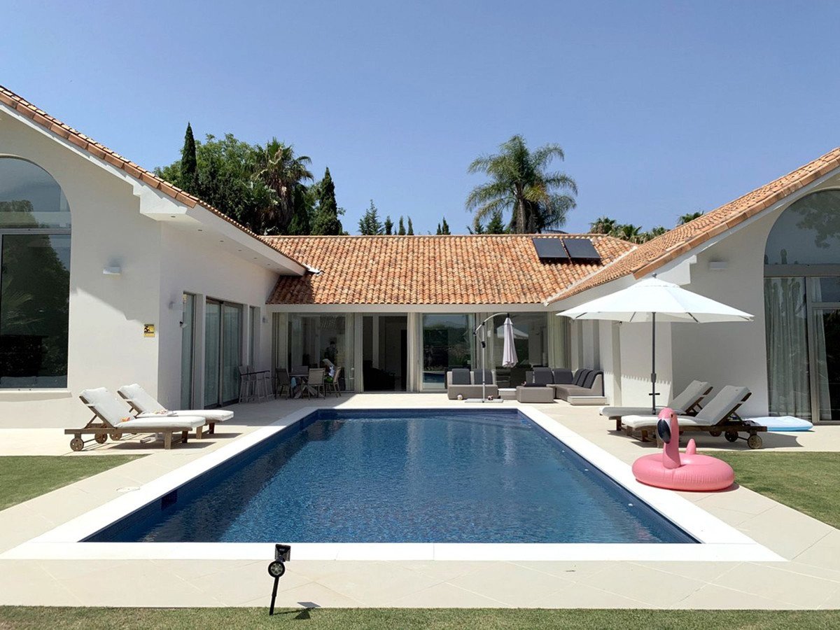 A modern villa with a swimming pool, lounge chairs, and an inflatable flamingo float on a sunny day.