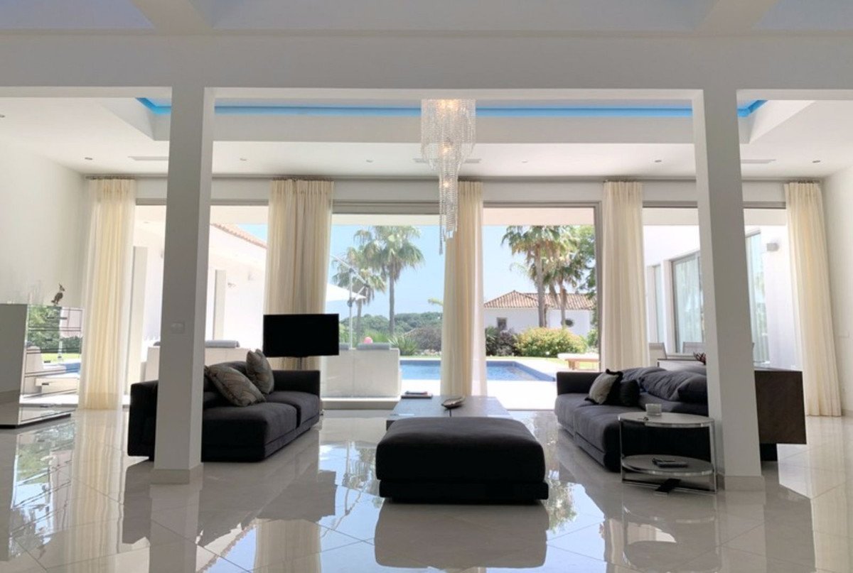 Spacious modern living room with sofas facing a pool and palm tree view through large glass windows.