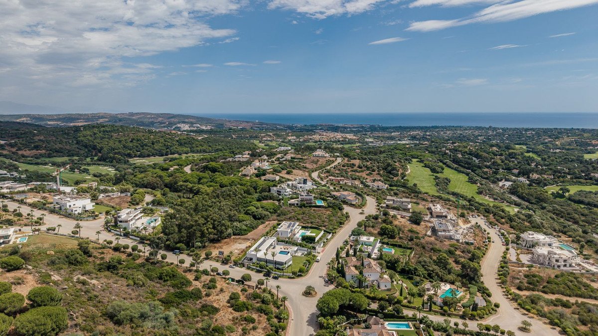 Aerial view of luxury villas with pools, nestled in a green landscape with a golf course and distant sea view.