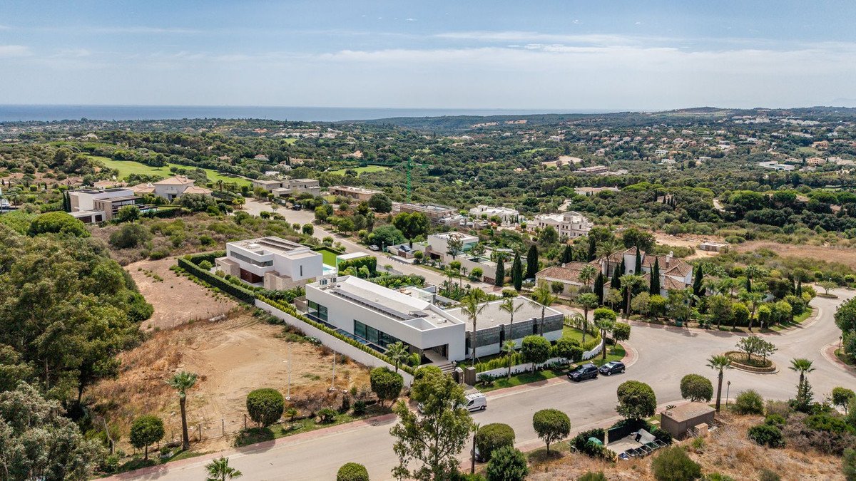 Aerial view of a modern white villa with a flat roof, set in a lush green landscape with distant sea views.