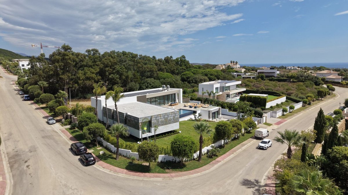 Modern luxury villa with a swimming pool and outdoor lounge area, overlooking the sea and surrounded by greenery.