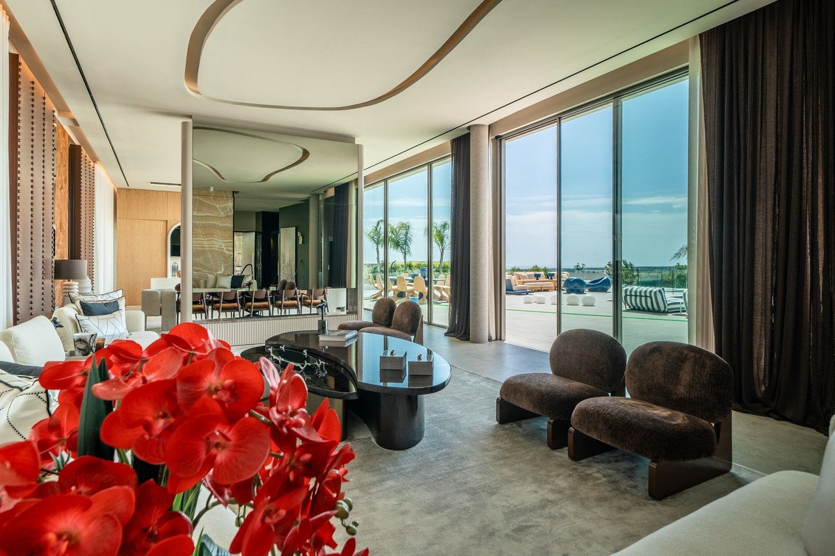 Modern living room with floor-to-ceiling windows offering an ocean view and access to an outdoor patio with seating.