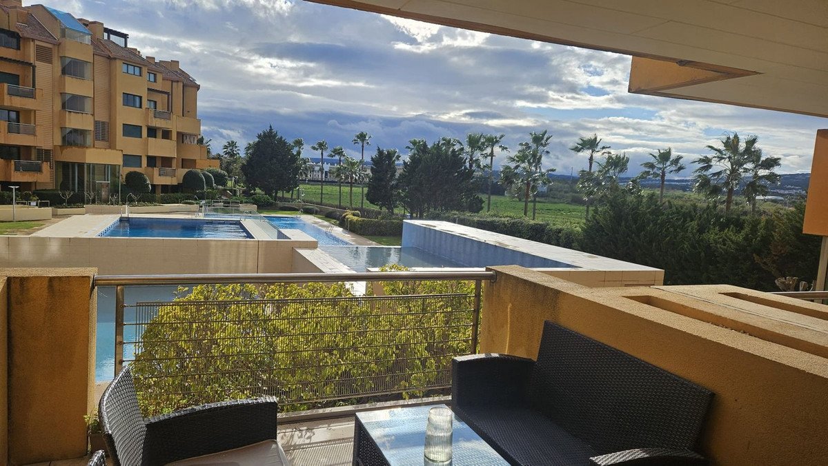 Balcony with seating overlooking a pool and garden with palm trees