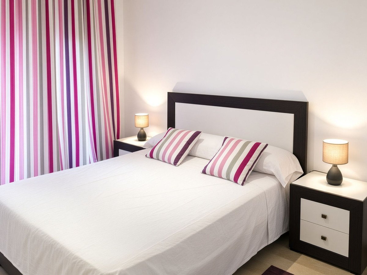 A bedroom with a double bed, two bedside tables with lamps, and brightly colored striped curtains.
