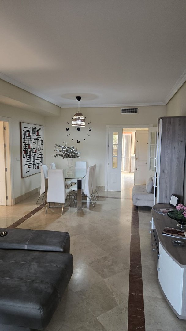 Modern open-plan living and dining area with tiled floors, white chairs, and artwork.
