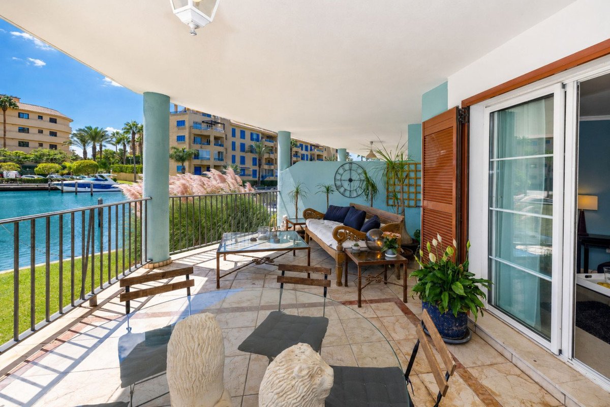 Spacious terrace with canal and boat view, furnished with seating area, overlooking palm trees and buildings.