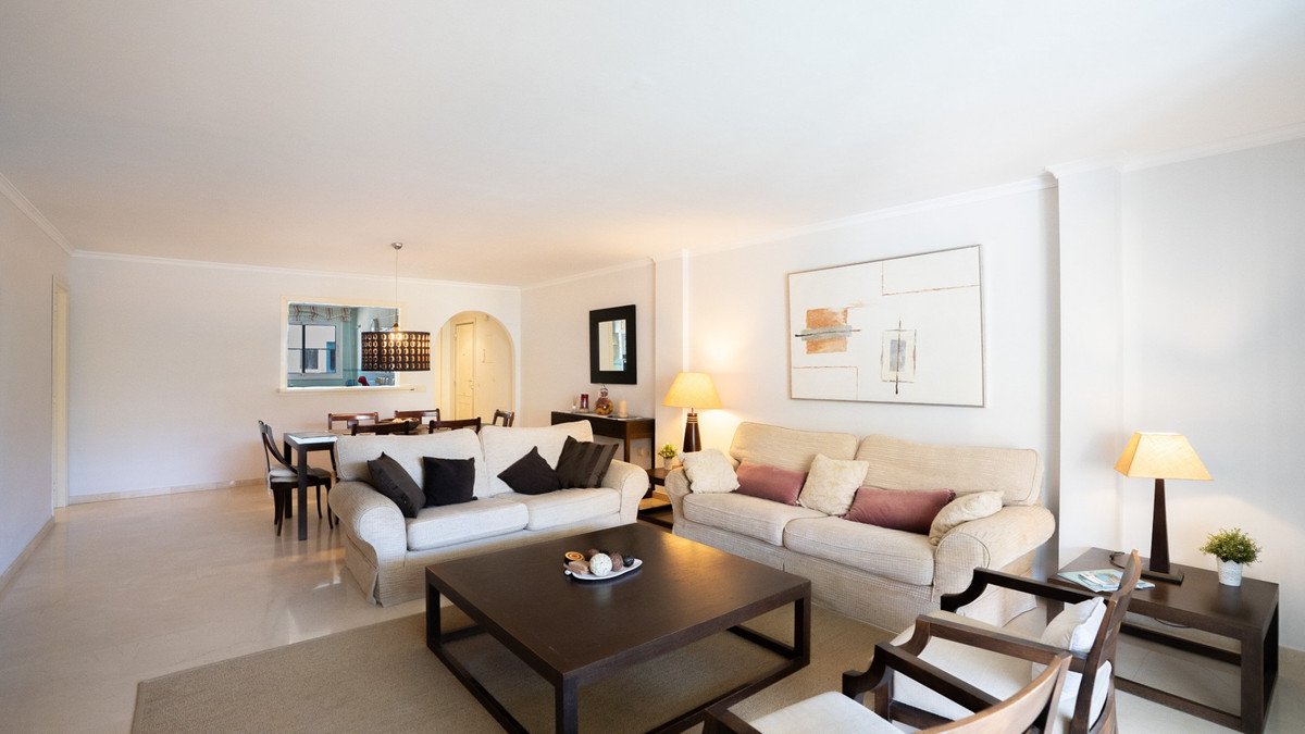 Spacious living and dining area with modern sofas, a large coffee table, and a dining set visible through a pass-through window.