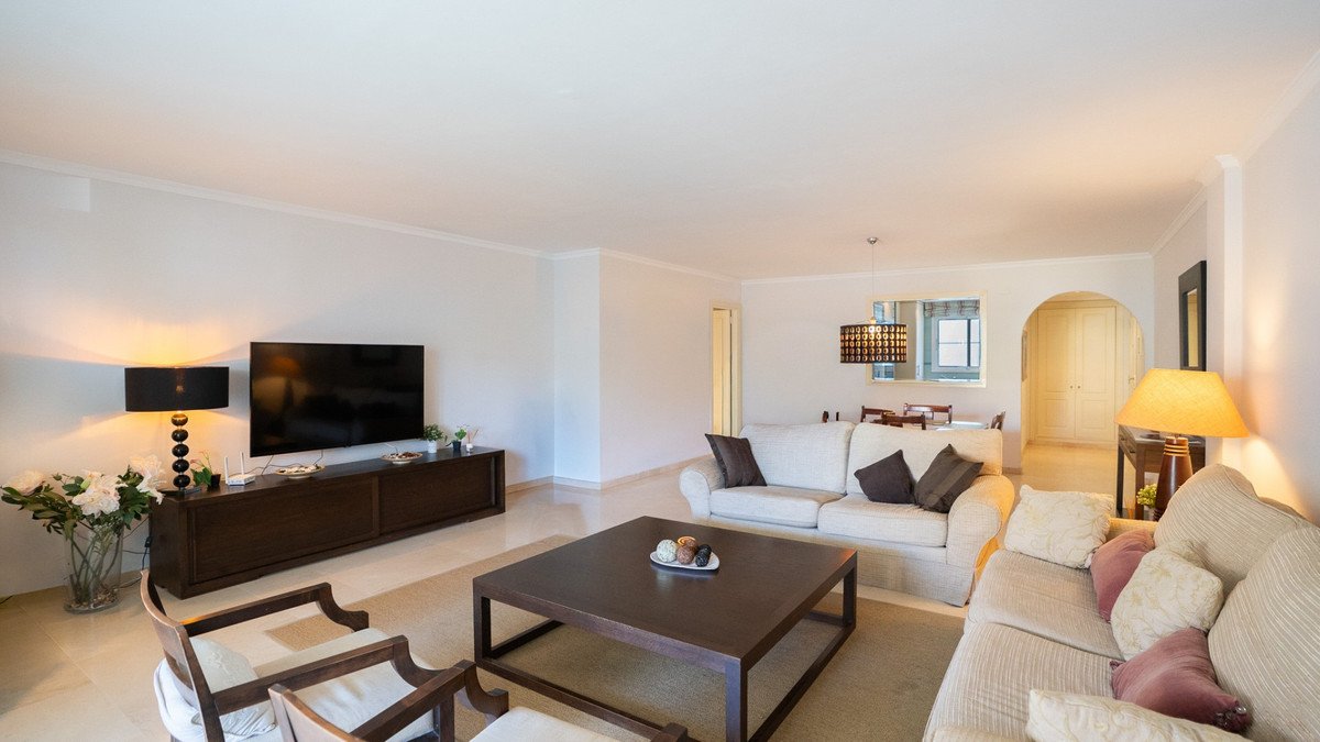 Spacious living room with two sofas, a large coffee table, a TV, and decorative lamps. An archway leads to another room.