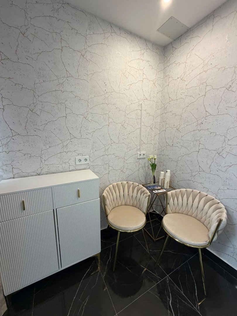 Modern waiting area with upholstered chairs, a white cabinet, and a glass side table with decorative items.