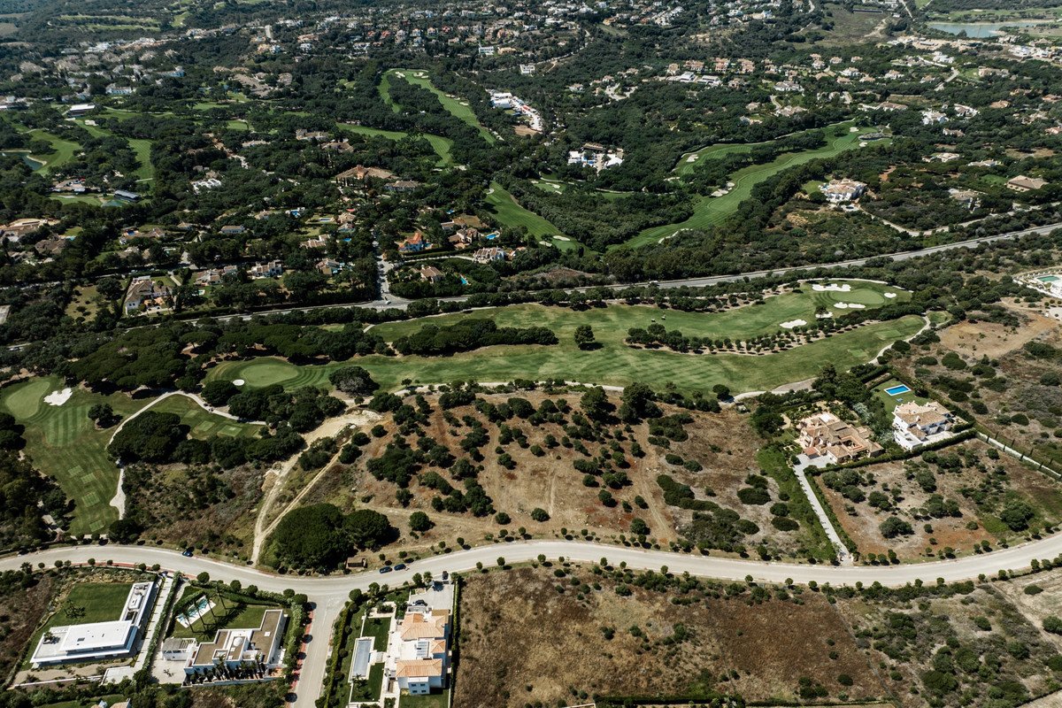 Aerial view of luxury villas overlooking a lush green golf course, surrounded by trees and residential areas.