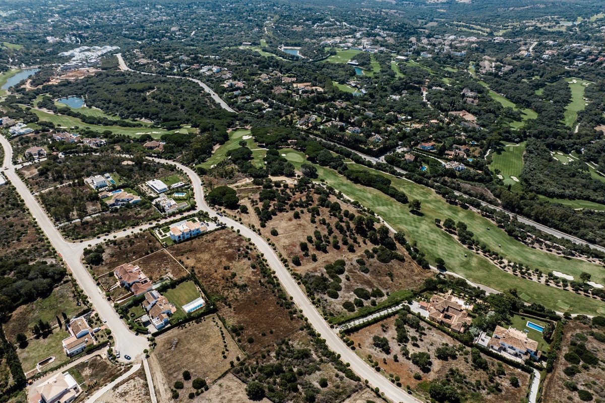 Aerial view of an estate with a golf course and trees, featuring multiple houses and swimming pools.