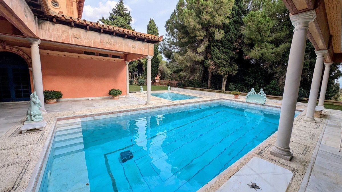 Outdoor swimming pool with columns and lush greenery in a villa setting