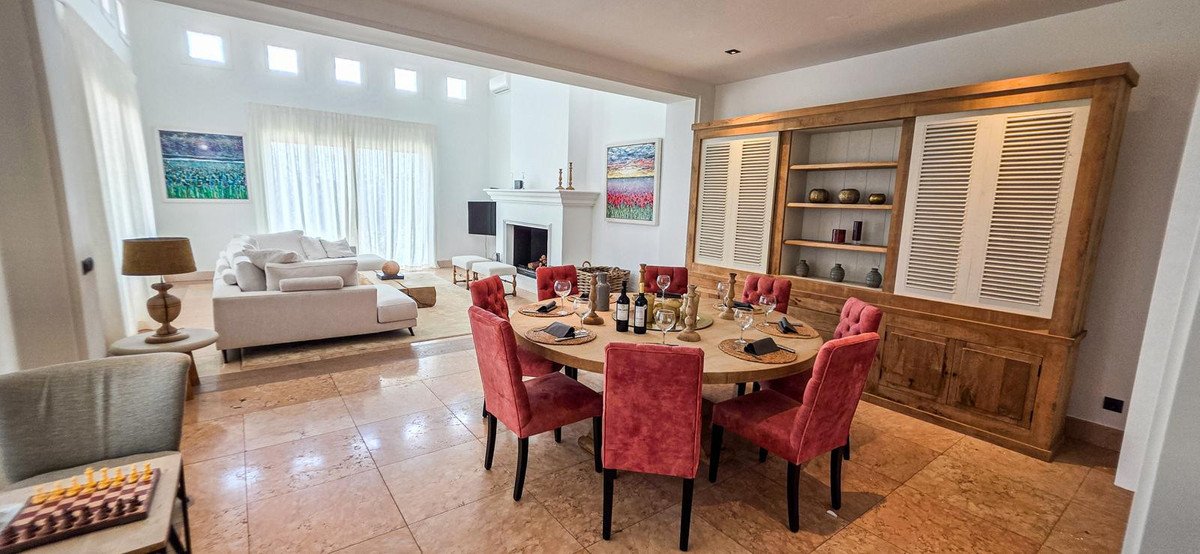 Elegant dining area with red chairs around a round table, adjacent to a modern living room with a large sofa.