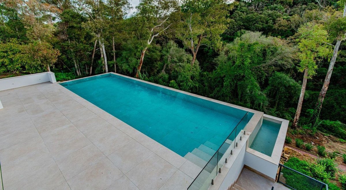 Modern infinity pool with a clear blue, calm water, surrounded by lush green trees and dense forest.