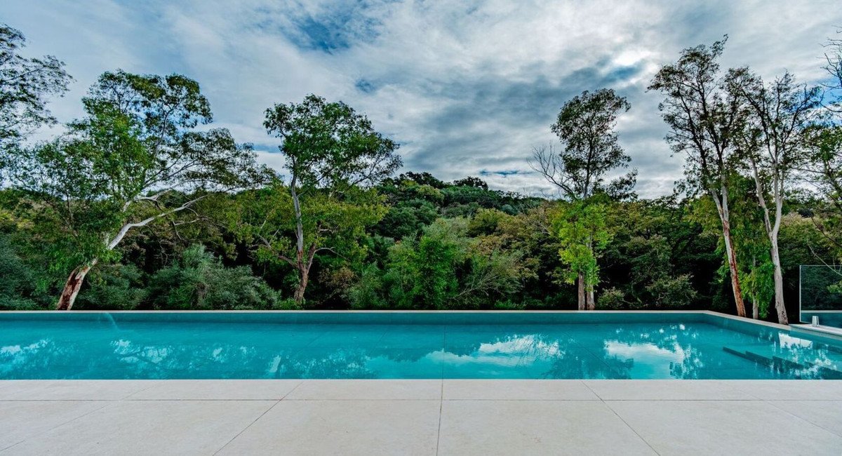 A modern infinity pool overlooking a dense, lush forest with cloudy skies overhead. Serene outdoor space.