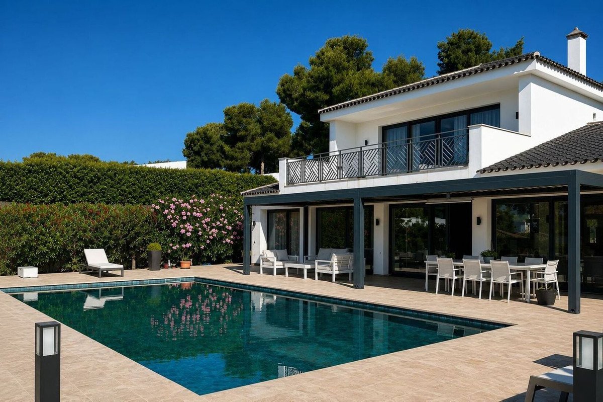 Modern white villa with a swimming pool, outdoor lounge area, and dining table on a sunny day.