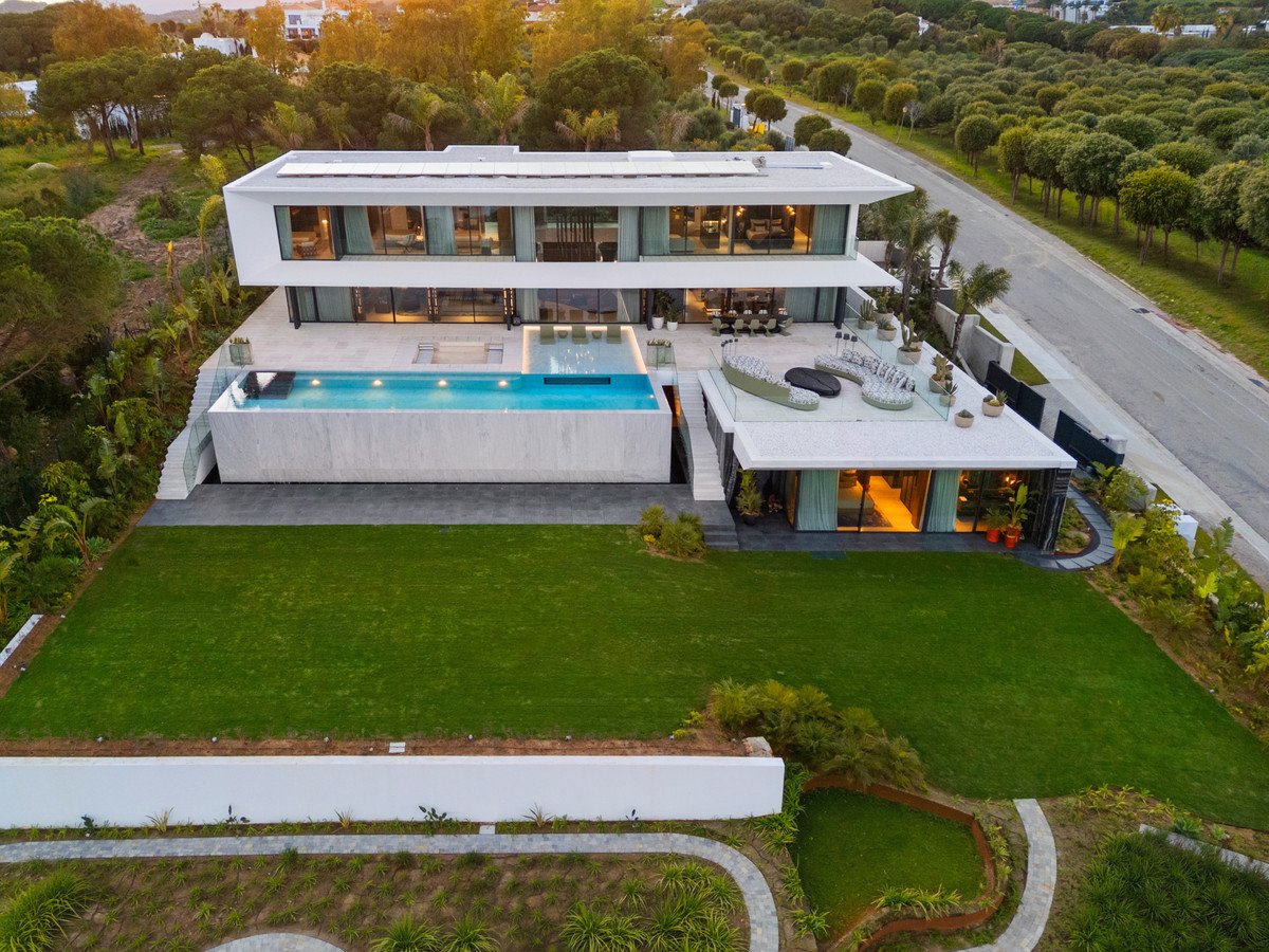 Modern villa with infinity pool, manicured lawn, and outdoor seating area during sunset.