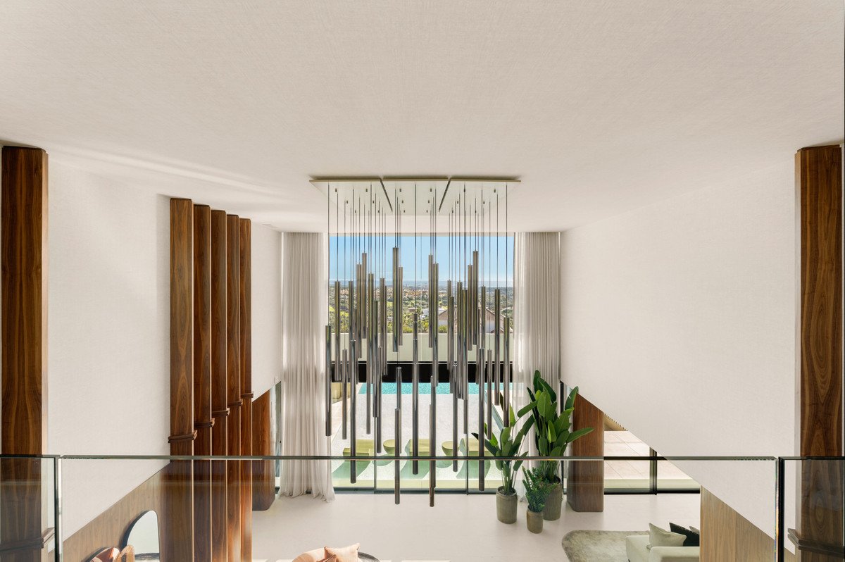 Modern interior balcony overlooking a swimming pool and cityscape, with a striking chandelier and wooden accents.