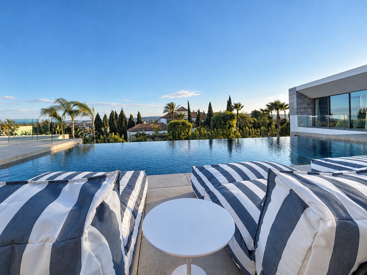 Luxurious infinity pool and lounge area with striped cushions overlooking the sea and surrounding landscape.