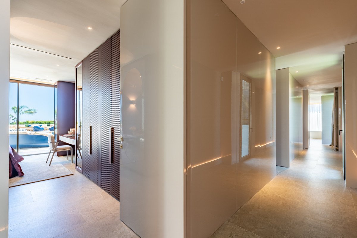 Hallway with modern wardrobes and a desk area, leading to a bedroom with a pool and palm tree view through large windows.