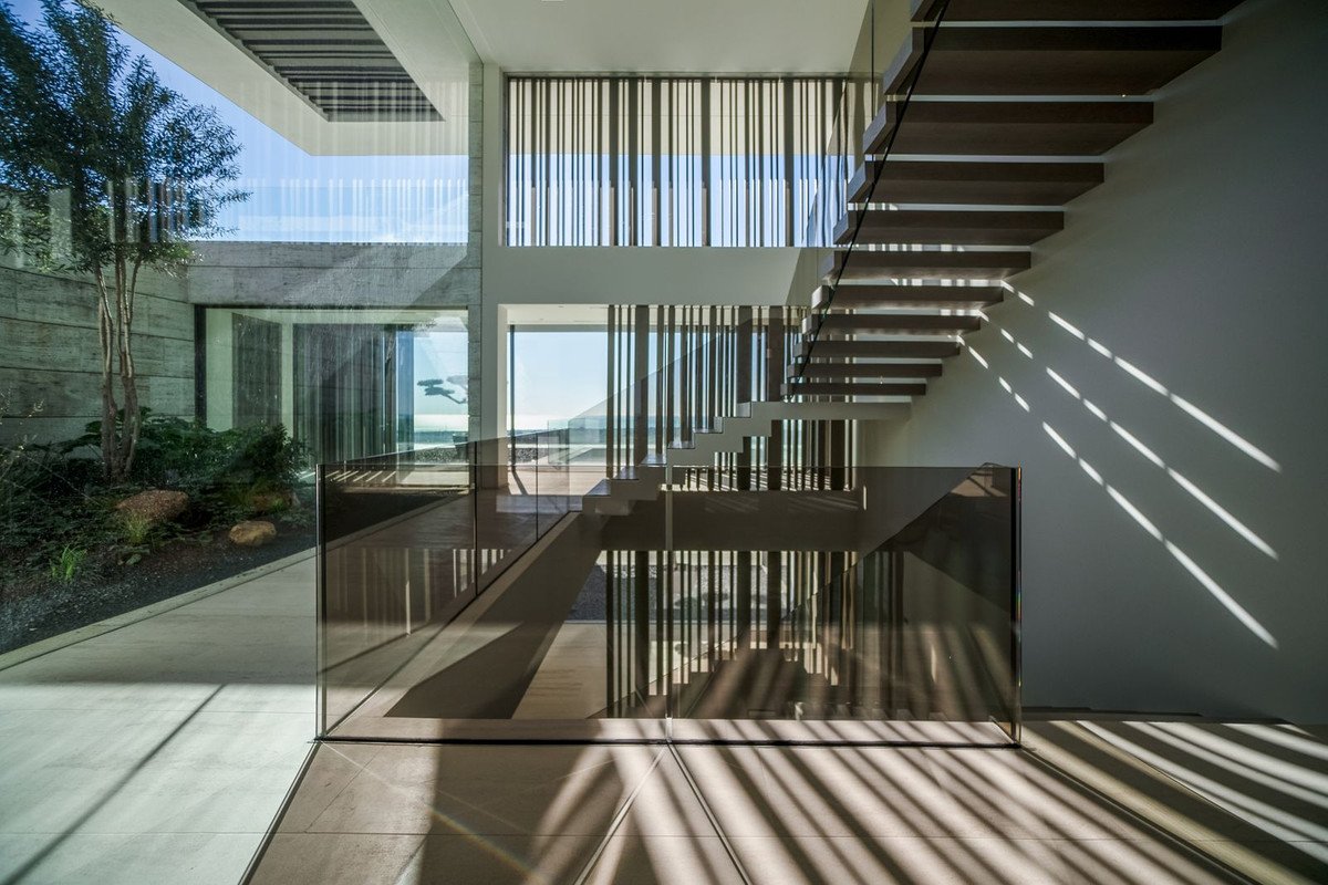 Modern floating staircase with glass balustrade, featuring natural light and a view of the sea.