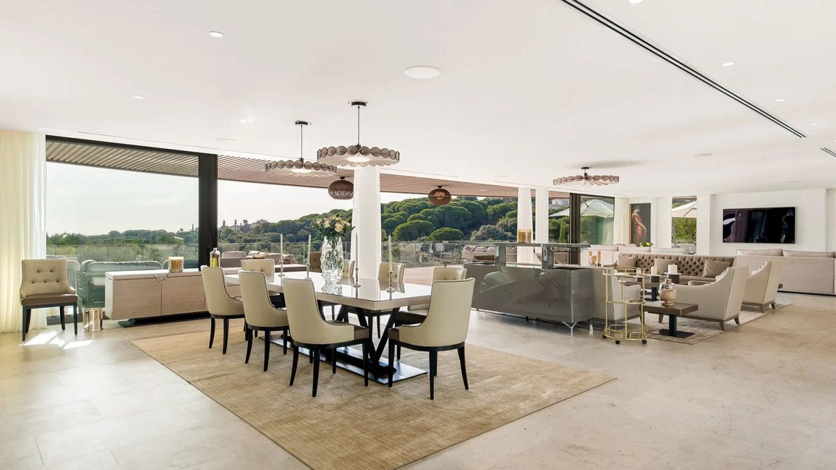 Spacious modern dining and living room with large windows offering a view of the sea and surrounding greenery.