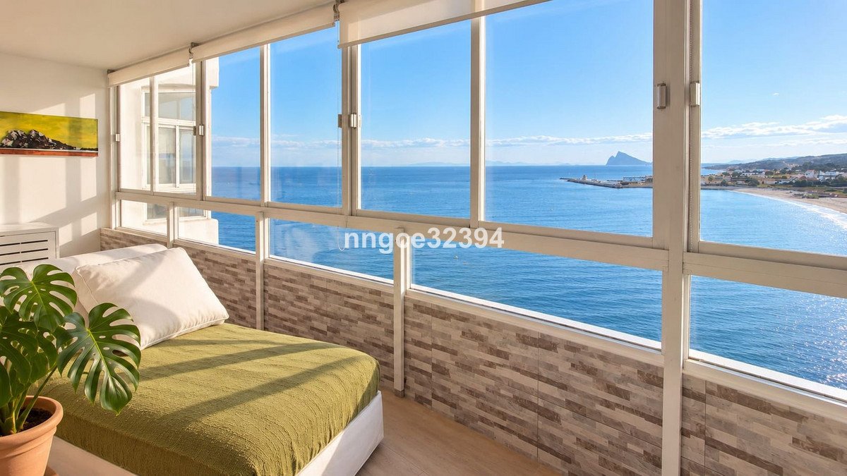 Modern sunroom with large windows offering a stunning sea view, overlooking a beach and distant coastline.