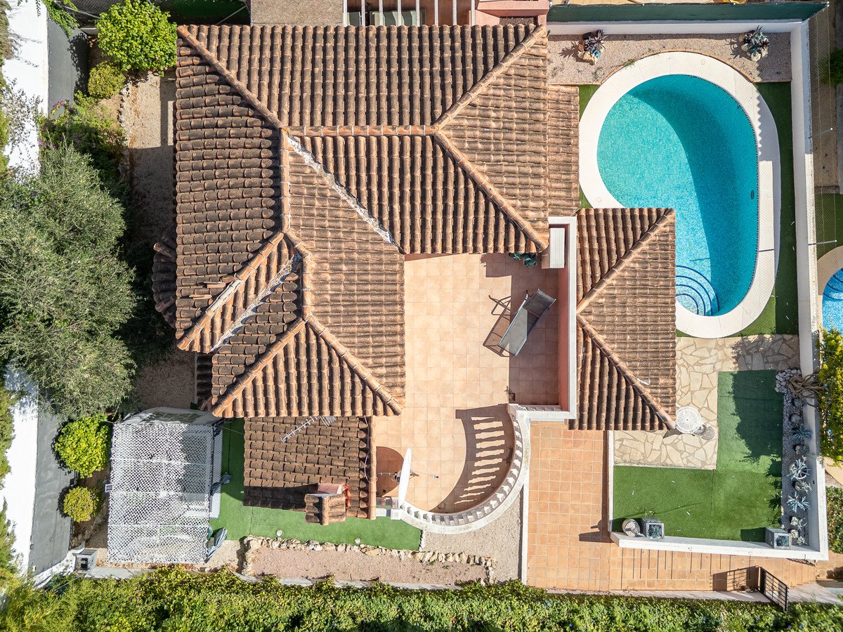 Aerial view of a villa featuring a swimming pool, patio, barbecue, and surrounding greenery.