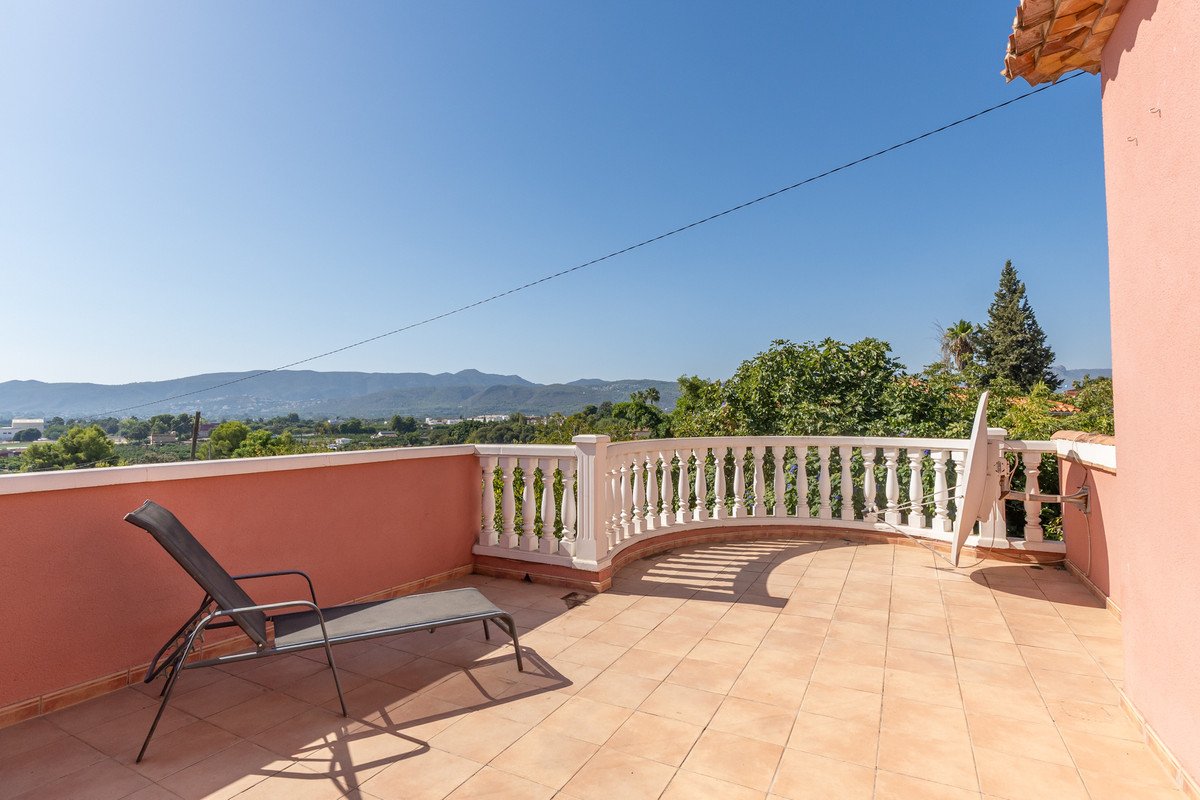 A sun lounger sits on a tiled terrace overlooking a scenic mountain landscape under a clear blue sky.