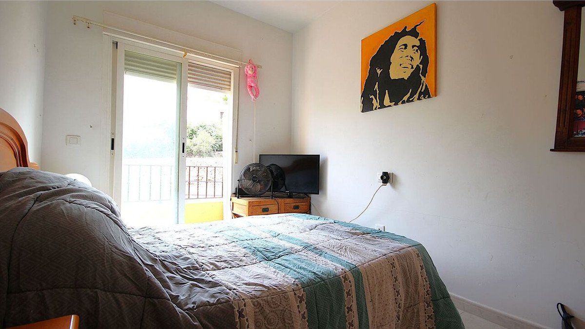 A bedroom with a bed, a balcony door leading to an outdoor space, and a Bob Marley painting on the wall.