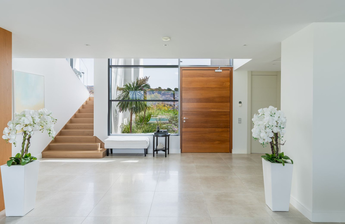 Moderne entreehal met houten trap en grote raampartij.